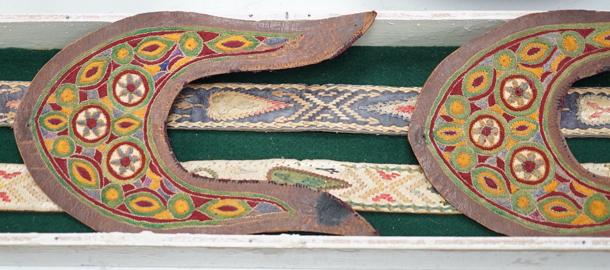 A two framed native American Indian ornately woven and embroidered leather belts and a pair of leather embroidered slipper fronts, longest belt 103cms